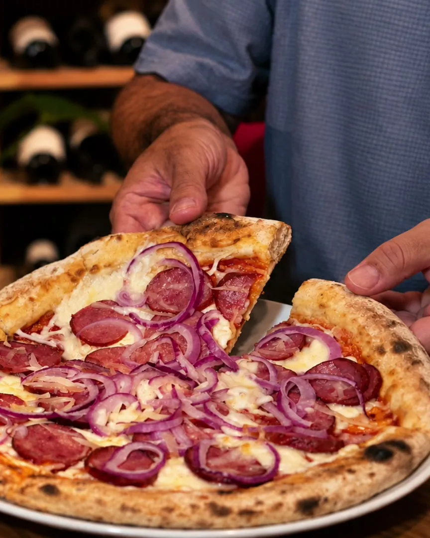 Pizza sendo servida com taça de vinho tinto ao lado